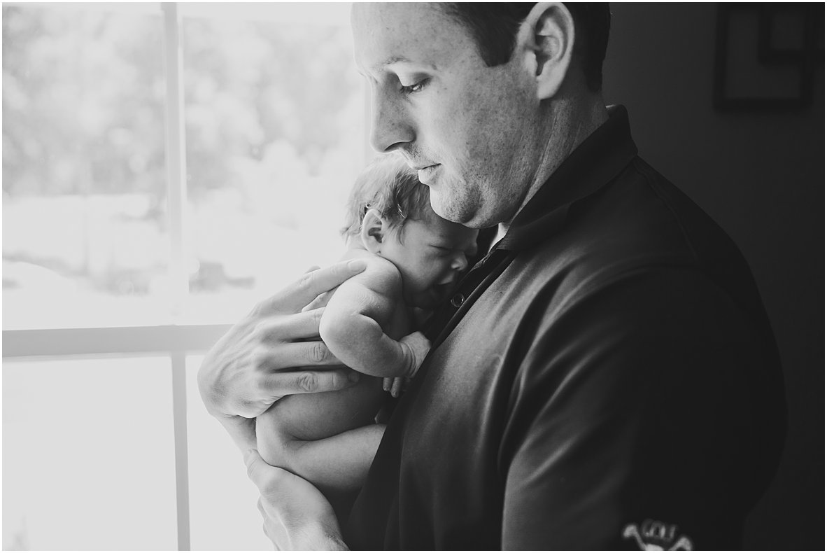 dad holding newborn in front of window