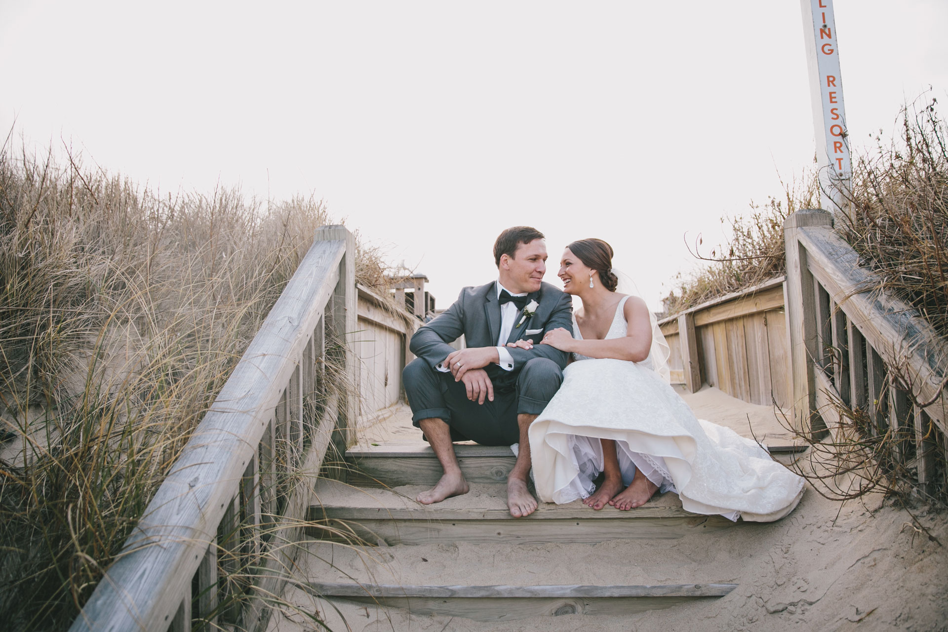 bride and groom sit on stairs on obx beach