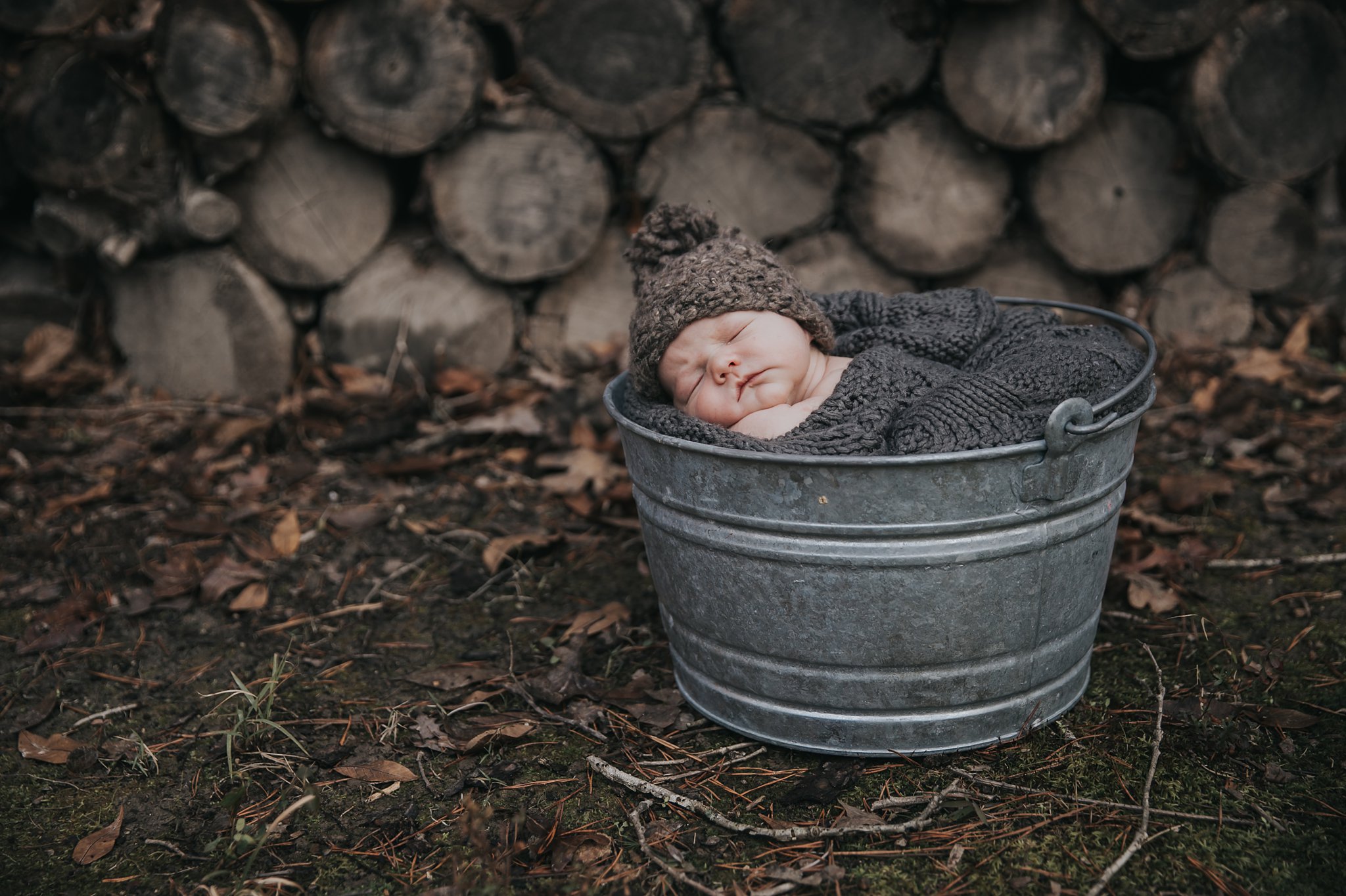 sleeping newborn boy outside in front of woodpile