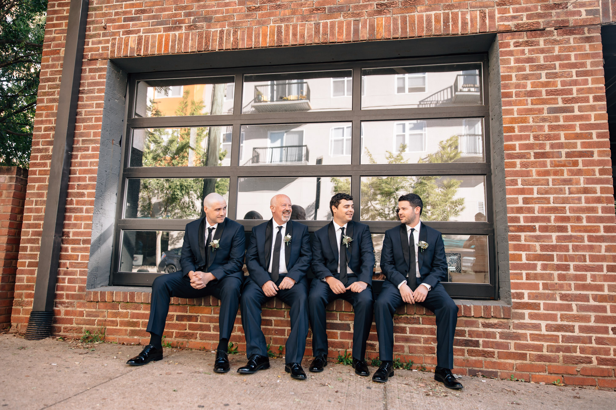 groomsmen sit on brick wall outside small wedding venue raleigh nc