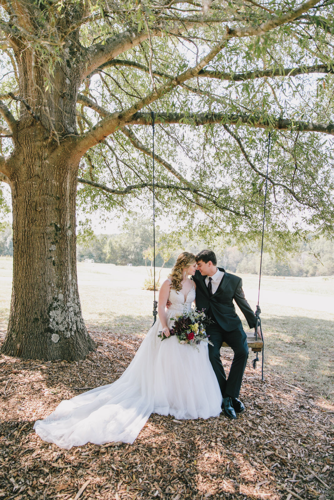 bride and groom sit on the tree swing at the meadows wedding venue